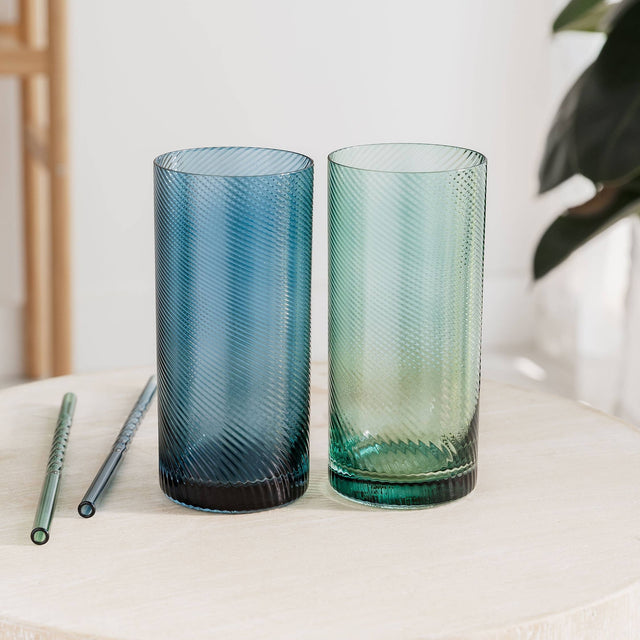 Two blue and green glass tumblers on a white surface with a blurred background