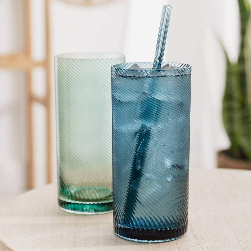 Two blue and green textured glasses with straws on a light surface.