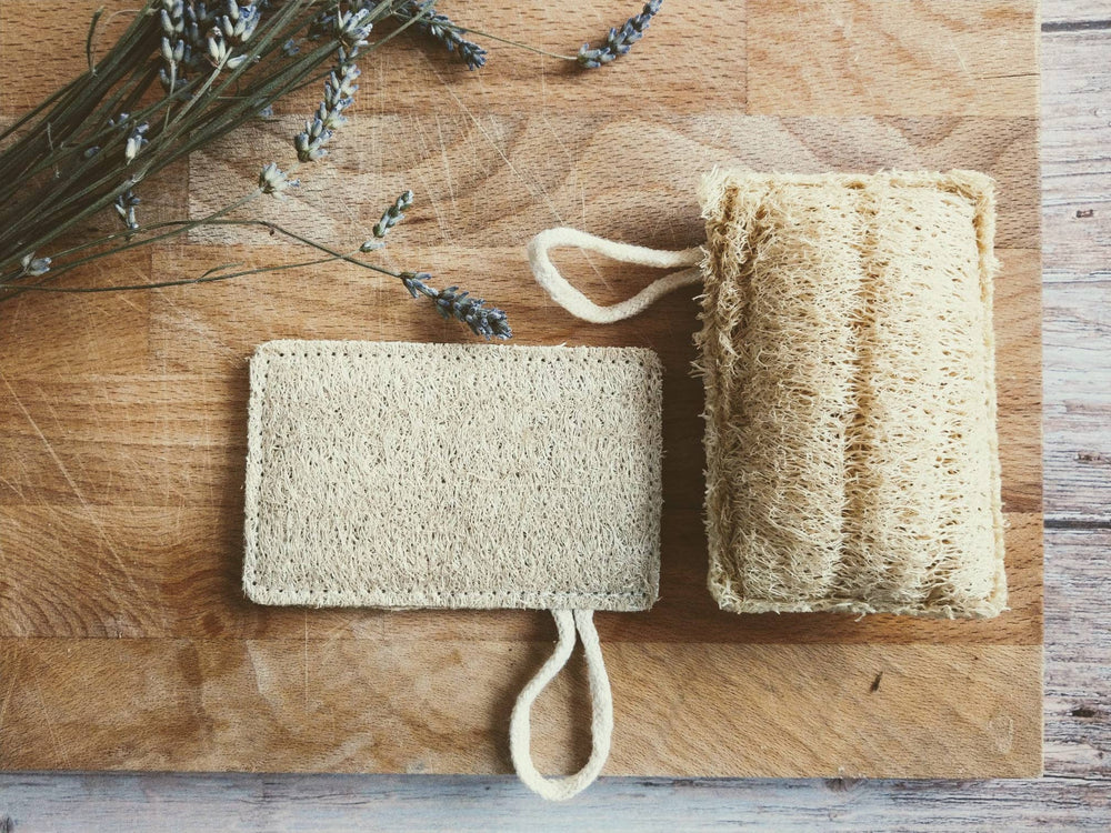 Two natural loofah sponges on a wooden surface with lavender flowers.