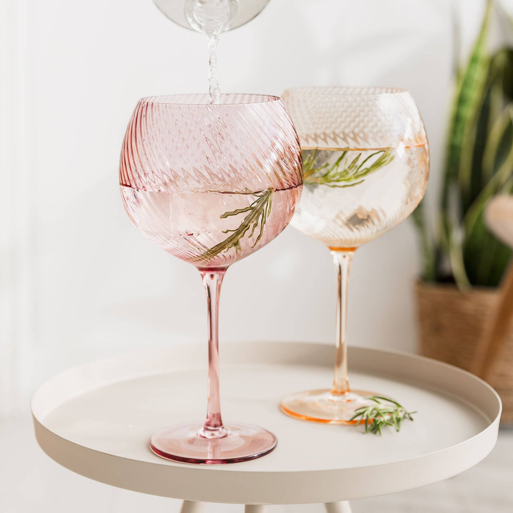Two pink and peach wine glasses with herb decorations on a white surface.