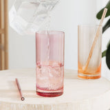 Two tall glasses with textured twist design on a light surface, one pink and one orange, with straws included.