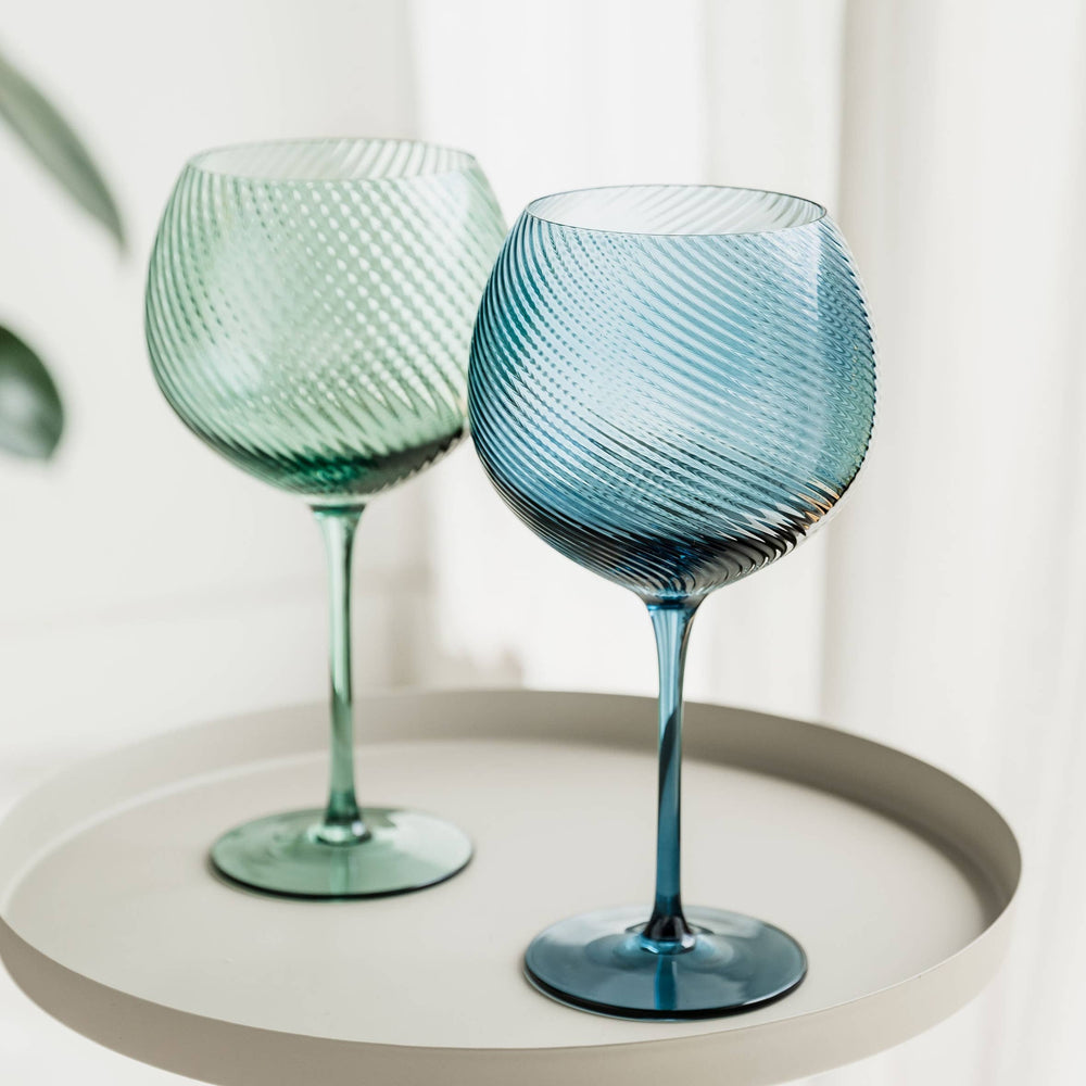 Two textured wine glasses on a round white surface with a light background