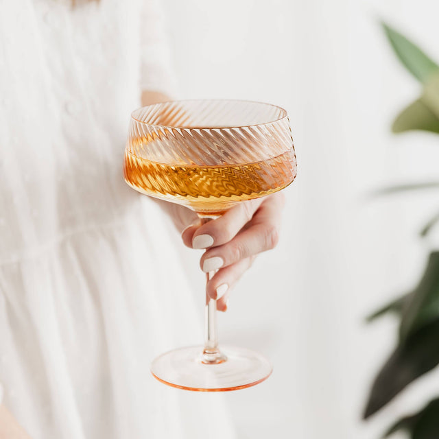 Hand holding a glass of orange liquid against a blurred background