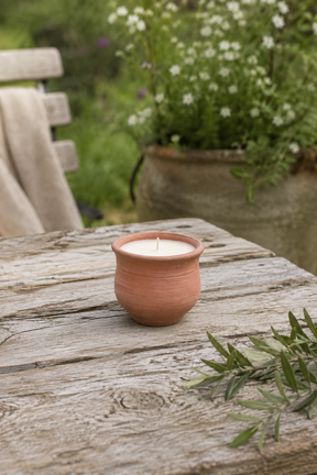 terracotta candle in a rustic terracotta pot on a wooden table with a garden background.