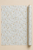 A roll of wrapping paper with a repeating pattern of Summer Dressed Girls in  illustrations on a Pastel Blue background, displayed next to a flat sheet of the same paper on a solid beige background.