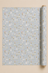 A roll of wrapping paper with a repeating pattern of Summer Dressed Girls in  illustrations on a Pastel Blue background, displayed next to a flat sheet of the same paper on a solid beige background.