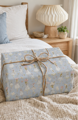 A wrapped gift box on a bed, covered in Vintage Fashion Sketch Wrapping Paper Pastel Blue and tied with natural twine.