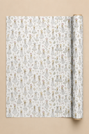 A roll of wrapping paper unrolled to show a repeating pattern of small illustrated girls in white dresses with floral details, set against a solid beige background.
