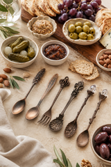 Assorted spoons and forks on a table with small bowls of pickles, olives, and other snacks.