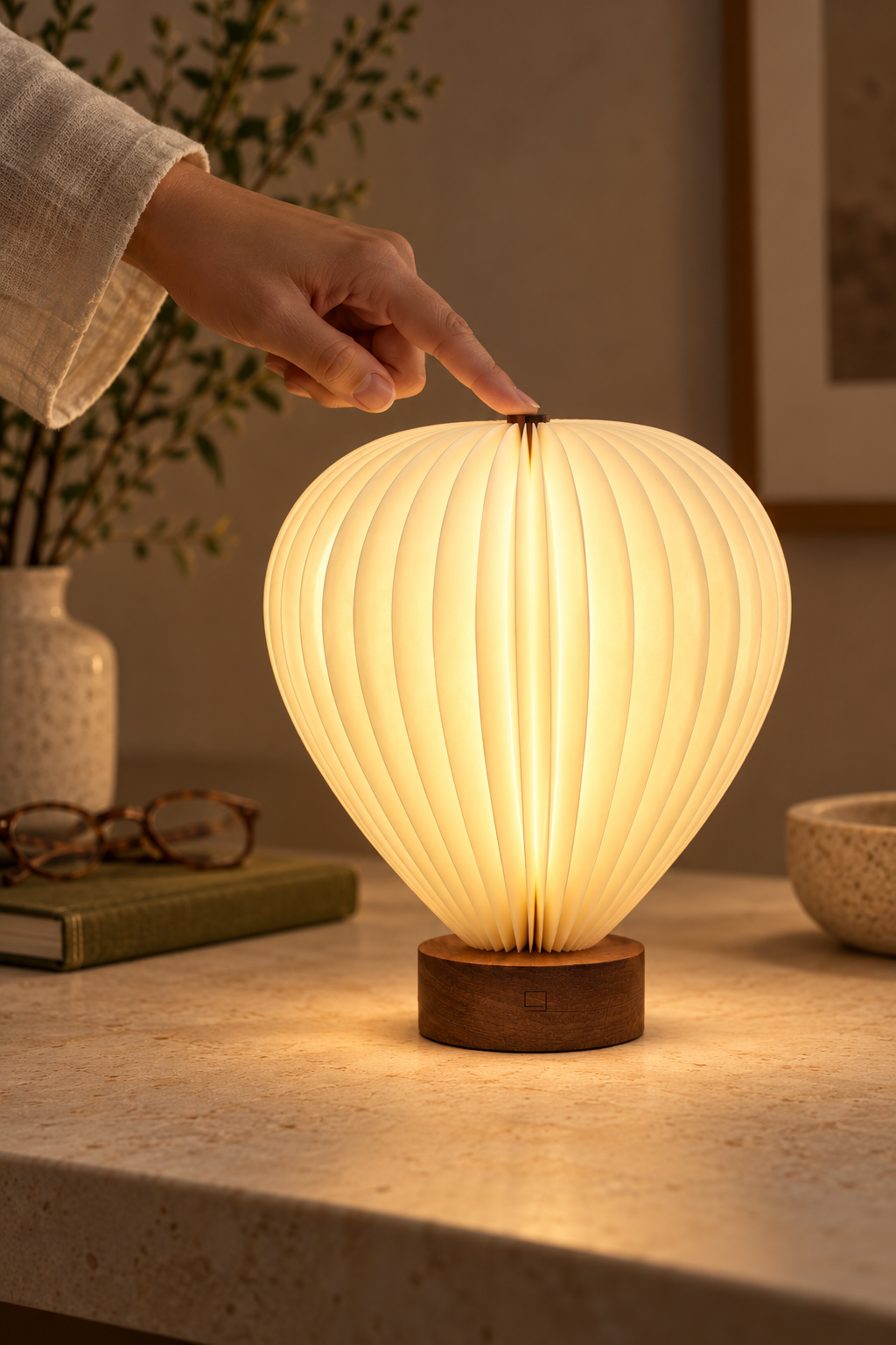 Hand touching the top control of an illuminated Aeris hot air balloon lamp with natural walnut wood base