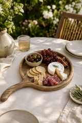 Walnut Wooden platter with assorted meats, cheeses, and grapes on a table outdoors.
