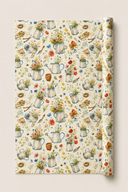 A roll of wrapping paper with a vintage watercolor pattern of watering cans, flowers, and gardening tools on a cream background, shown partially unrolled.
