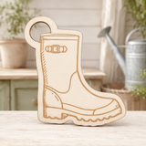 A wooden boot-shaped decorative plaque or sign with engraved details, standing on a light wooden surface with a softly blurred garden-themed background.