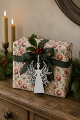 Ornate white angel gift tag on a Holly & Bauble wrapped Christmas present with green linen ribbon and fresh holly.