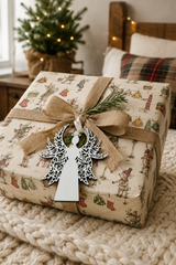 White filigree angel gift tag tied to a Reindeer Washing Day wrapped present in a cosy Christmas bedroom.
