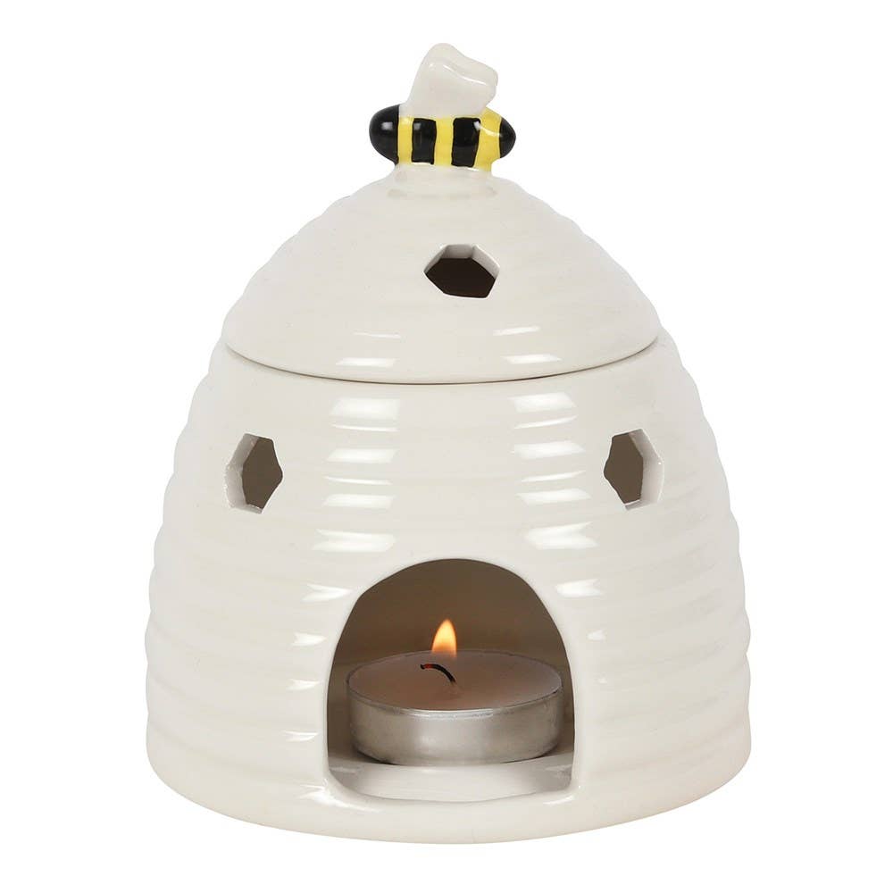 White ceramic beehive-shaped oil burner with a lit candle inside on a white background