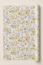 A roll of wrapping paper featuring a repeating watercolor-style pattern of Mediterranean hillside houses in warm beige, white, and soft blue tones, shown against a light neutral background.