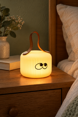 Mochi Wonder lamp with wide eyes glowing on an oak bedside table beside linen bedding.