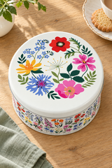 A round floral tin cake box, shown on a wooden table with its lid leaning behind it in a bright kitchen 