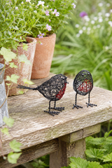 Decorative wire birds on a wooden surface with plants in the background