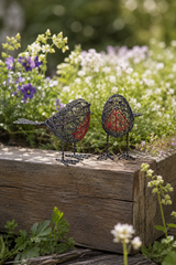 Two wire bird sculptures on a wooden surface with flowers in the background