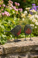 Two wire bird sculptures on a stone ledge with flowers in the background