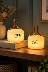 Mochi Wonder and Peek lamps glowing on a wooden shelf against a blue-green panelled wall.