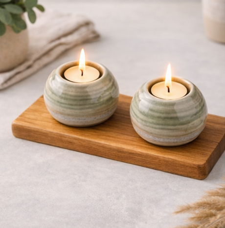 Two lit candles in ceramic holders on a wooden tray with a neutral background