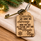 A wooden Christmas key tag engraved with the phrase 'Santa, WE HAVE NO chimney HERE YOU SEE SO PLEASE JUST USE THIS Magic Key' and a snowflake, shown with a brass key on a burlap fabric with holiday lights in the background.