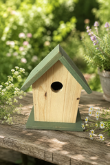 Wooden birdhouse with green roof on a wooden surface with flowers and plants in the background