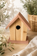 Wooden birdhouse with pink roof on a wooden surface with plants in the background