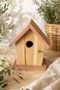 Wooden birdhouse with pink roof on a wooden surface with plants in the background