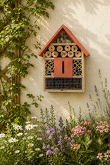 Insect hotel attached to a wall with flowers and plants in the foreground