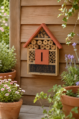Wooden bee hotel attached to a wooden wall with plants around
