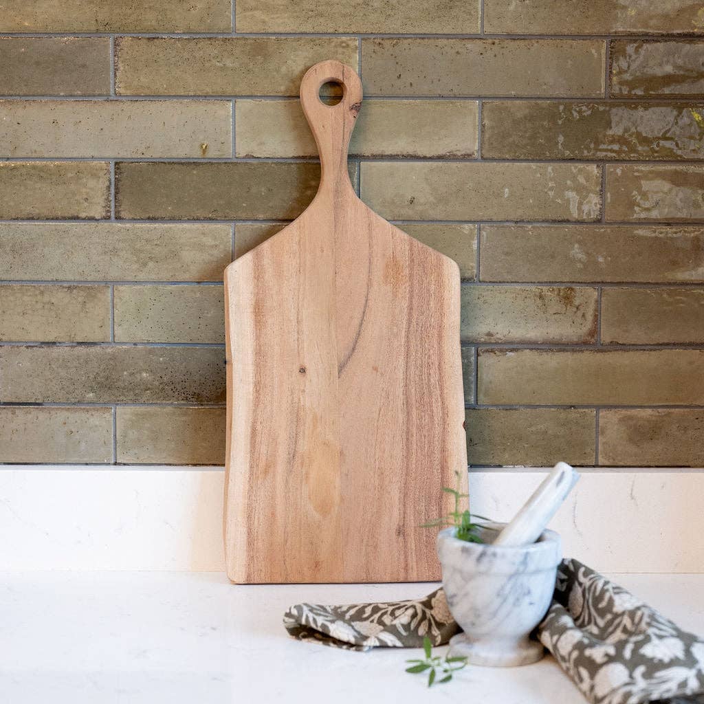Wooden cutting board with a handle against a brick wall.