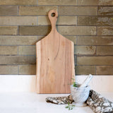 Wooden cutting board with a handle against a brick wall.