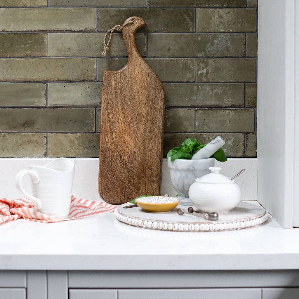Wooden cutting board on a kitchen counter with a stone wall background