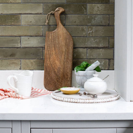 Wooden cutting board on a kitchen counter with a stone wall background