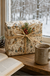 Illustrated woodland animal Christmas wrapping paper featuring scarf-wearing foxes, rabbits and mice sharing hot drinks and mince pies at a winter garden party. The pencil-sketch design includes lanterns, wrought-iron tables, watering cans, holly and snowy branches in teal, russet, pink, mustard, red and green on warm ivory.