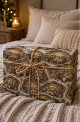 Detailed woodland Christmas wrapping paper showing badger families sharing a Boxing Day supper inside snow-covered underground burrows. The illustrated design includes lanterns, puddings, teapots, baskets, pantry shelves and holly in an earthy brown, cream, red, green and snowy white palette.