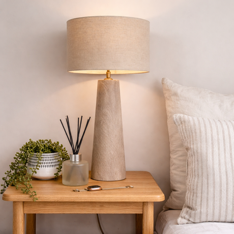 Beige table lamp on a wooden side table with decorative items, next to a sofa.
