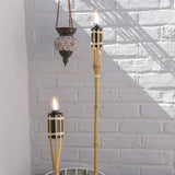 Two lit tiki torches with a hanging lantern against a white brick wall.