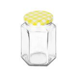 Clear glass hexagonal jar with a yellow checkered lid on a white background