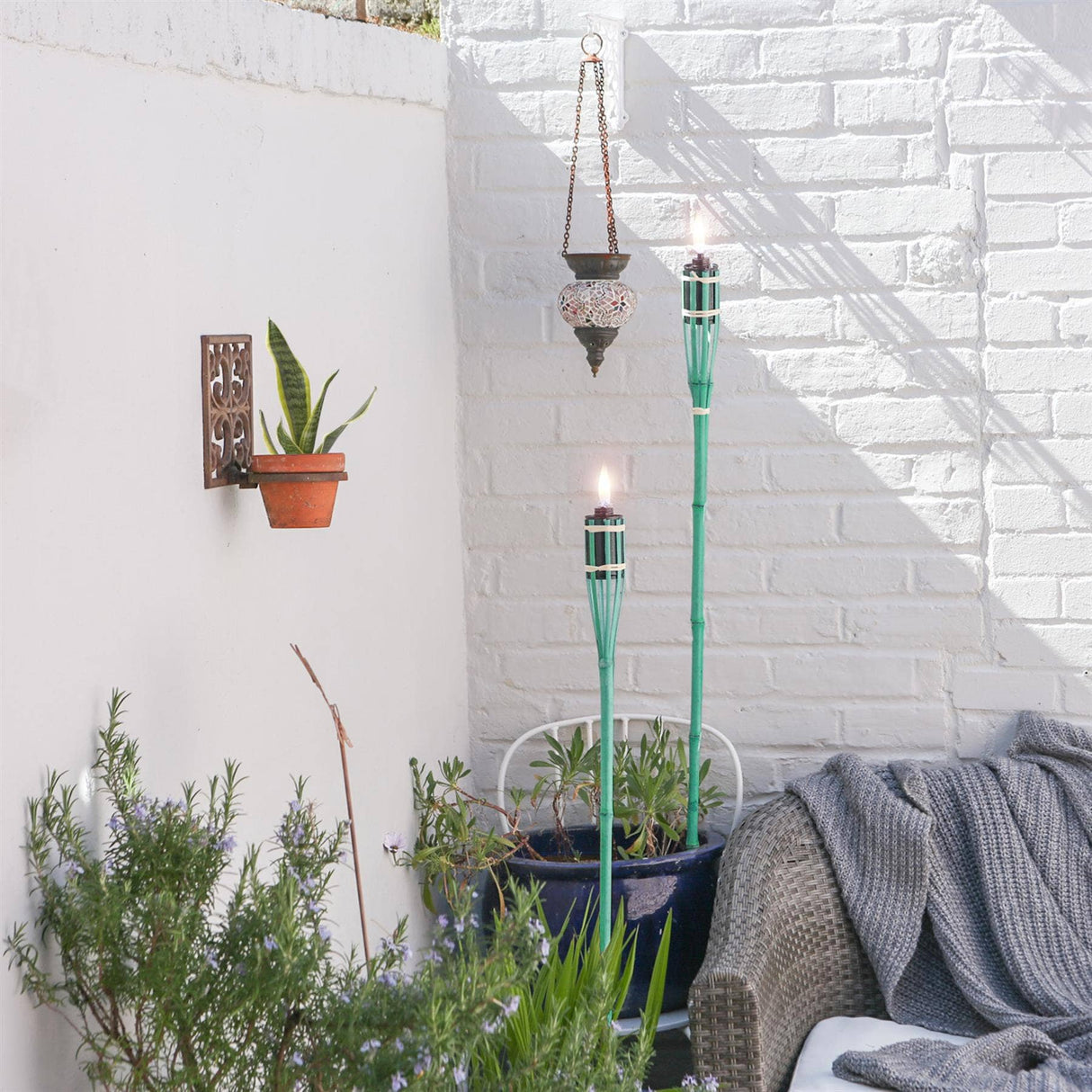 Outdoor setting with tiki torches, plants, and a white brick wall.