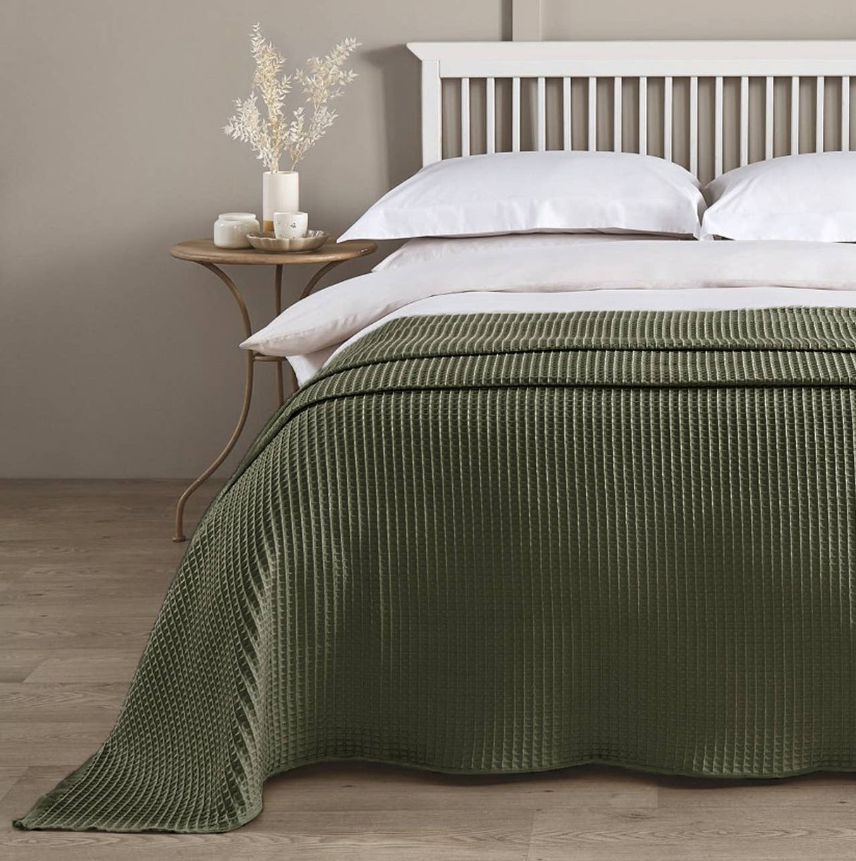 Bed with green blanket and white pillows in a room with a wooden nightstand and decorative items.