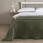 Bed with green blanket and white pillows in a room with a wooden nightstand and decorative items.