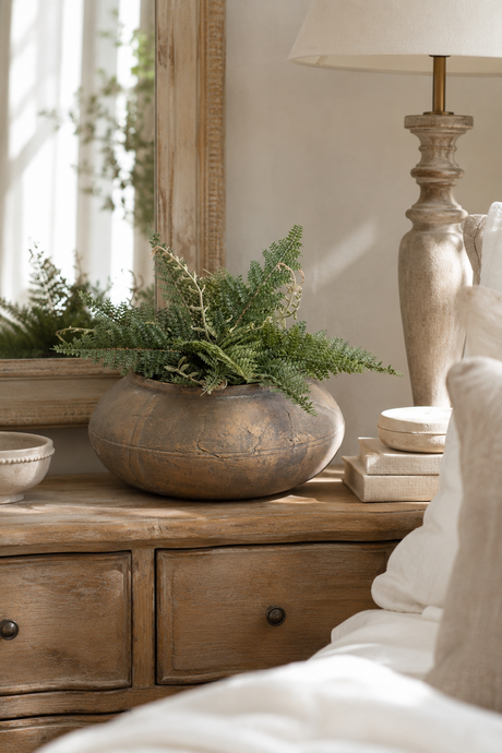 Baybridge plant pot on a wooden side table with a fern plant, lamp, and books in a cozy room setting.