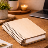 Wooden notebook on a wooden table with a candle and plants in the background