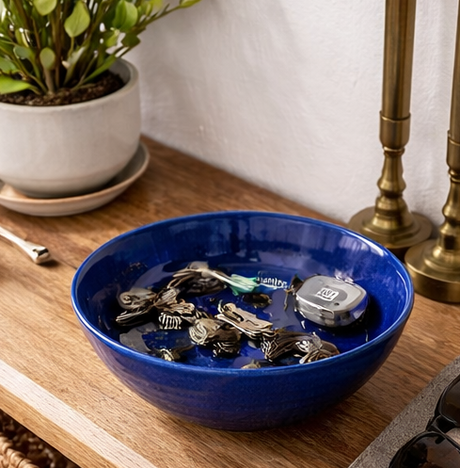 Blue bowl filled with keys on a wooden surface next to a plant and lamp.