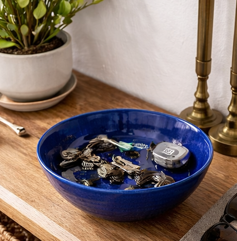 Blue bowl filled with keys on a wooden surface next to a plant and lamp.
